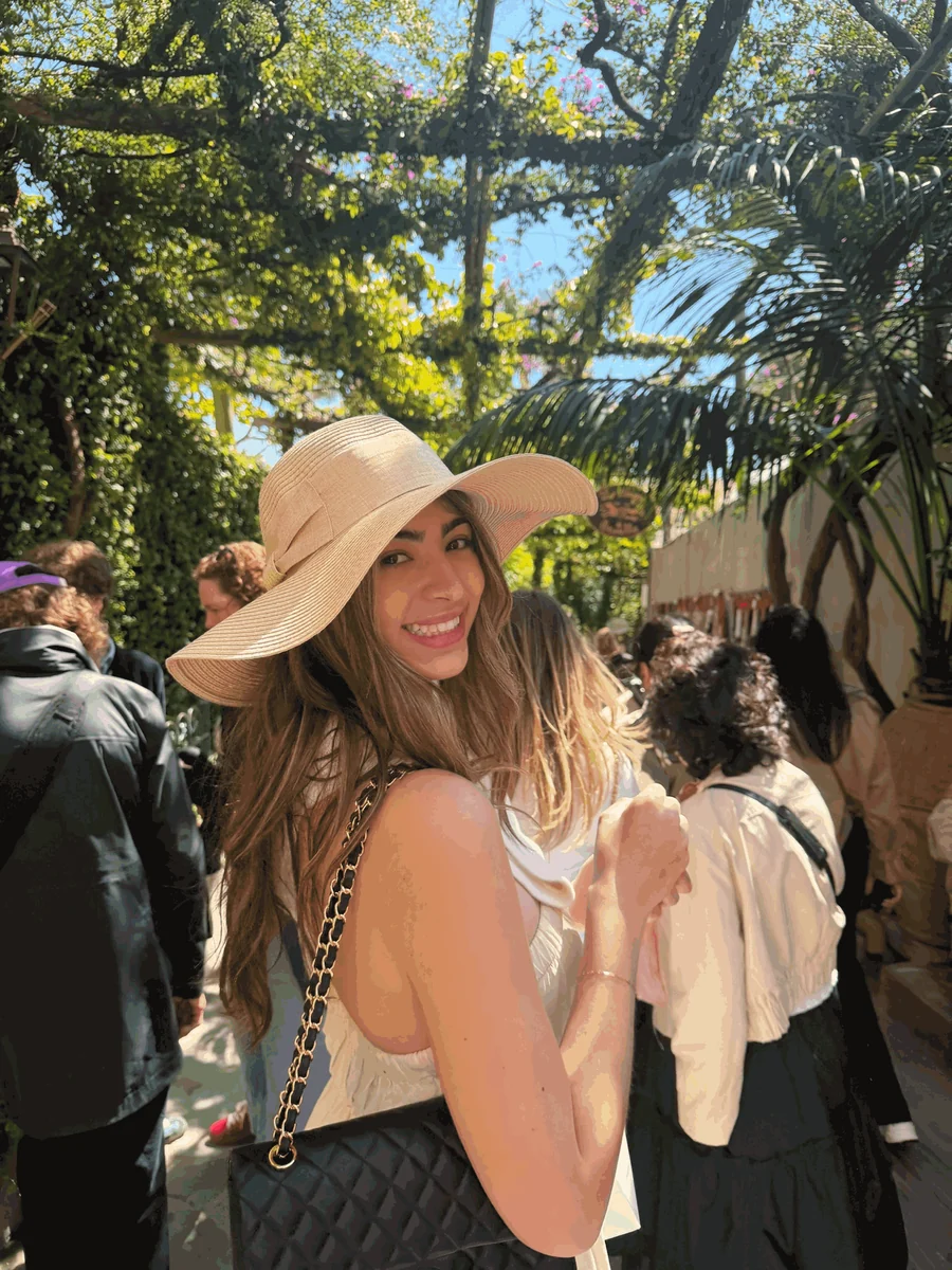 Jordyn smiling in a wide-brimmed sun hat under a canopy of trees while traveling